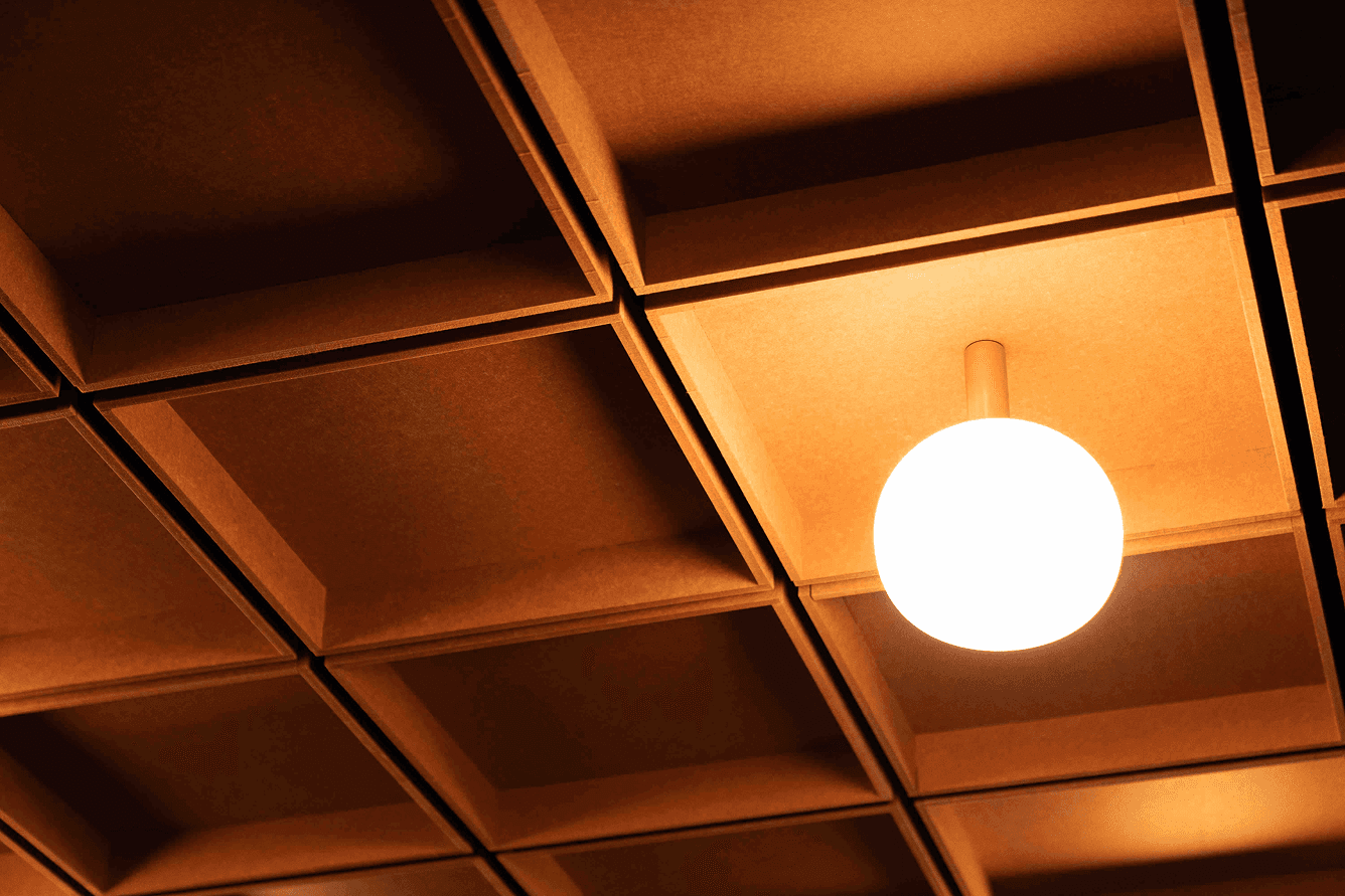 Warmly lit, square wooden panel ceiling with a glowing round light fixture hanging from the center.