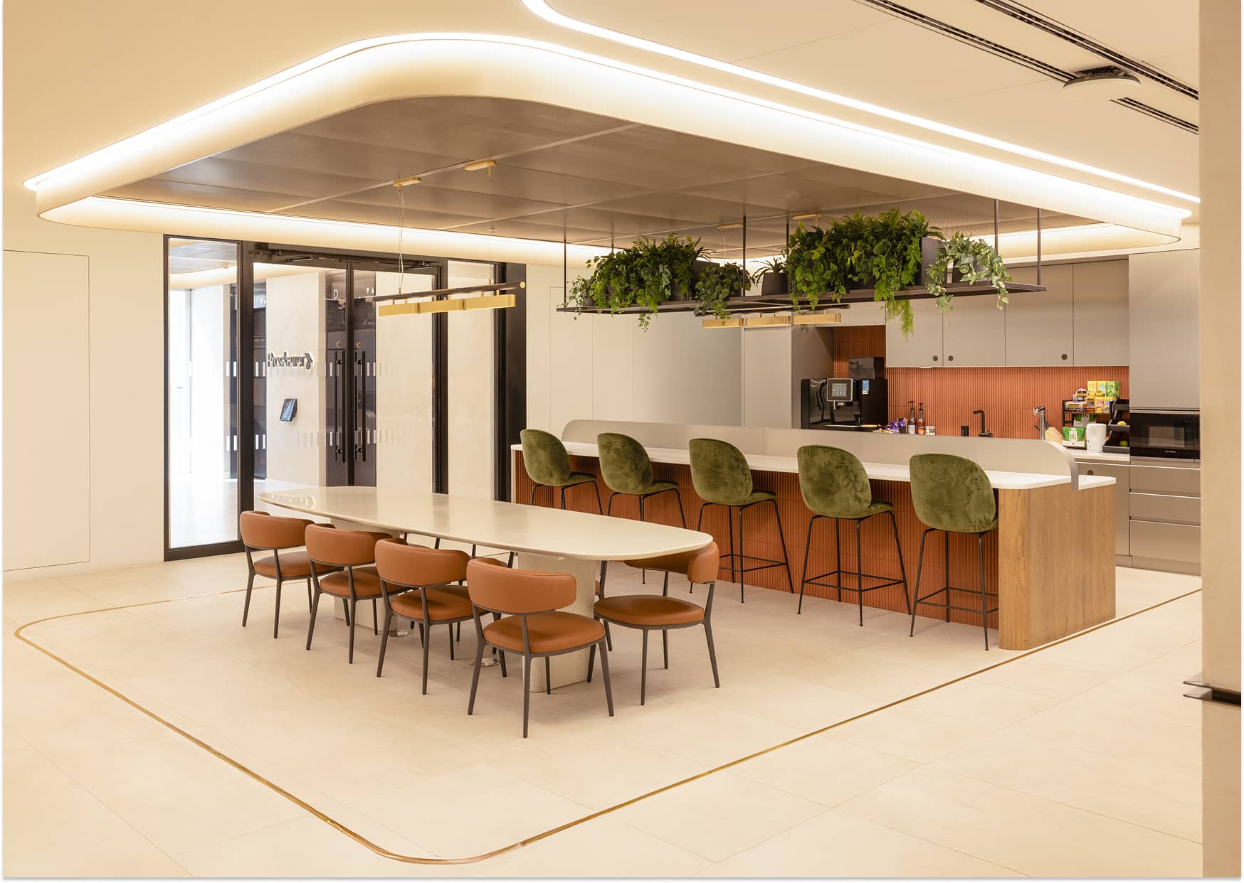 Modern office kitchen with a long dining table, brown chairs, bar stools, overhead greenery, and sleek lighting.
