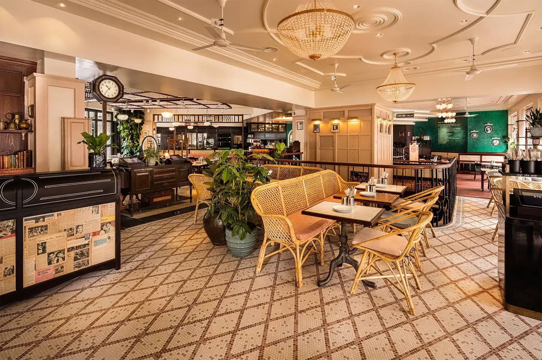 Elegant restaurant interior with wicker chairs, patterned tiled floor, chandeliers, and a cozy ambiance. Green plants and vintage decor accents the space.