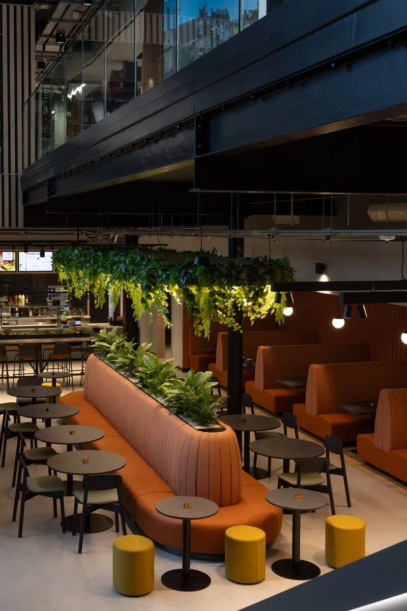 A shot of a communal working space, with integrated furniture planting at the centre and hanging planting above